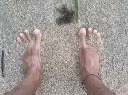 Persona caminando descalza por la playa al atardecer practicando grounding en verano